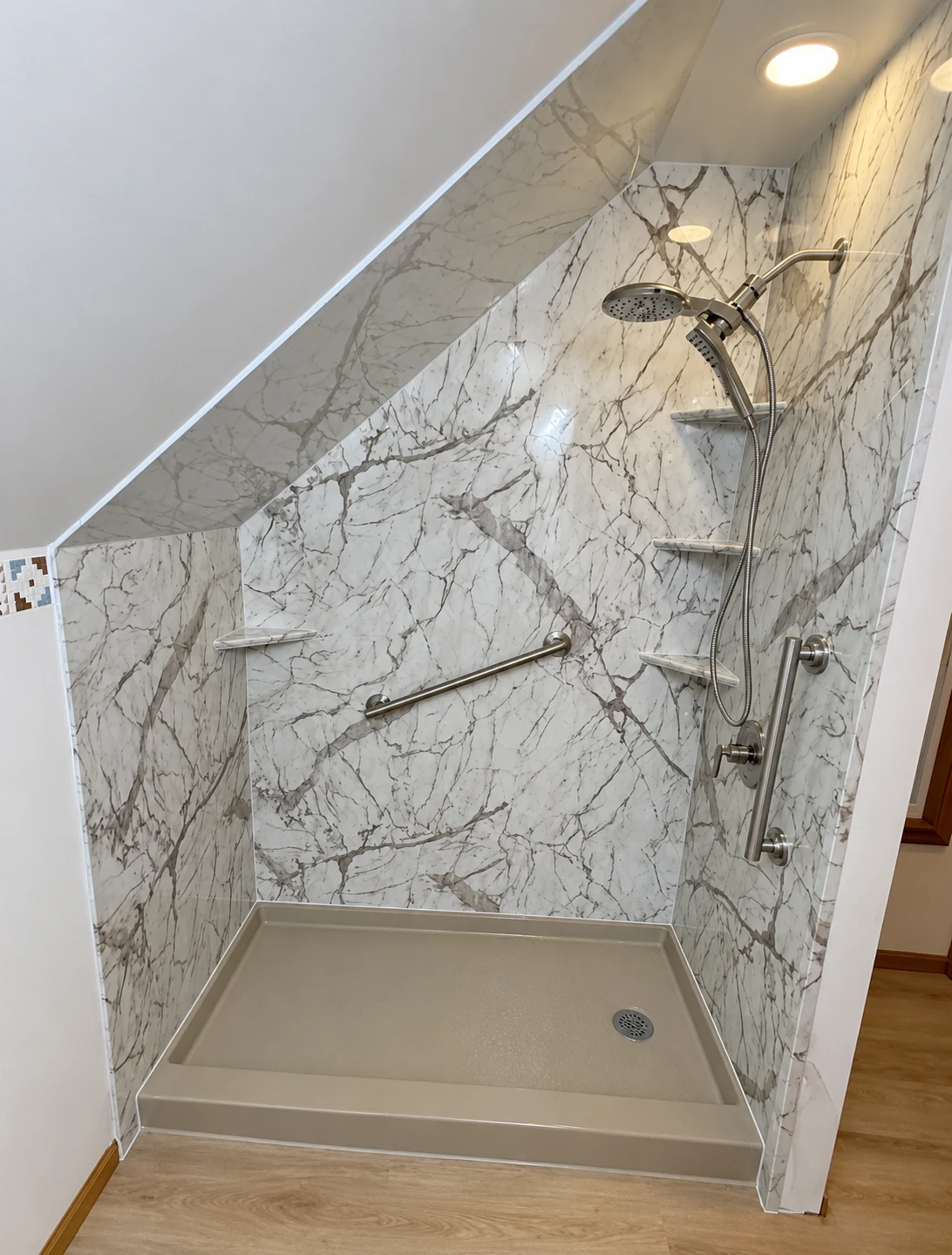 Marble-look shower fitted beneath a sloped ceiling with brushed metal fixtures